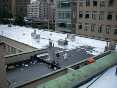 Our team applying fully adhered seamless elastomeric roof coating on a flat roof
