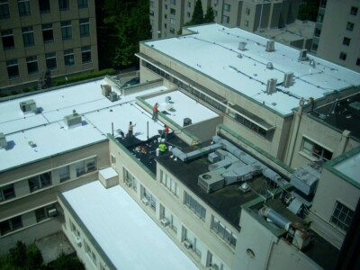 The Leewens Corporation team applying a roof coating to a large commercial flat roof.