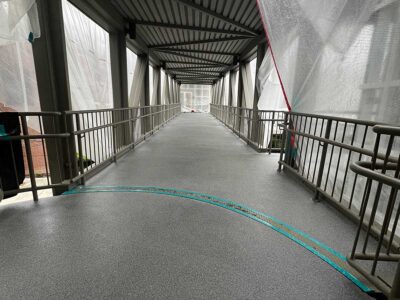 Newly installed resinous flooring on the Bellevue Square Skywalk, showing the textured gray surface and surrounding metal railings. Newly installed resinous flooring on the Bellevue Square Skywalk, showing the textured gray surface and surrounding metal railings.