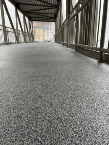 Close-up view of newly installed resinous flooring on the Bellevue Square Skywalk, showing the textured gray surface and surrounding metal railings.
