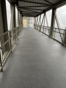Long view of the Bellevue Square Skywalk with smooth gray resinous flooring extending between metal railings under a covered walkway. Long view of the Bellevue Square Skywalk with smooth gray resinous flooring extending between metal railings under a covered walkway.