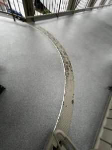 Curved metal traction strip embedded in a gray textured walkway, bordered by railings. Curved metal traction strip embedded in a gray textured walkway, bordered by railings.