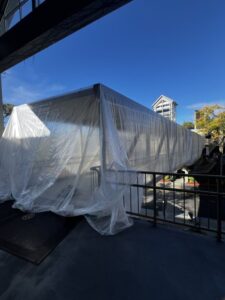 A large structure covered in clear plastic sheeting outdoors under a bright blue sky. A large structure covered in clear plastic sheeting outdoors under a bright blue sky.