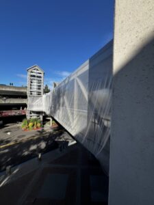 A skybridge covered in plastic stretches between buildings on a sunny day, with clear blue sky above. A skybridge covered in plastic stretches between buildings on a sunny day, with clear blue sky above.