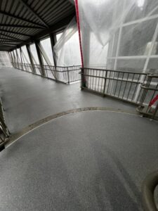 A covered pedestrian walkway with metal railings and translucent plastic sheets on the sides. A covered pedestrian walkway with metal railings and translucent plastic sheets on the sides.