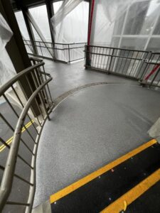 Curved section of the Bellevue Square Skywalk featuring fresh resinous flooring near a stairway with yellow safety striping and metal handrails.
