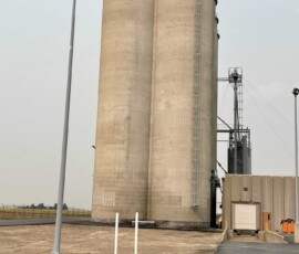 Two tall concrete grain silos standing next to a warehouse building.