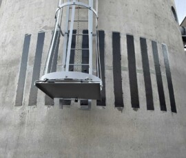 A metal ladder attached to a concrete structure with vertical black reinforcement strips.