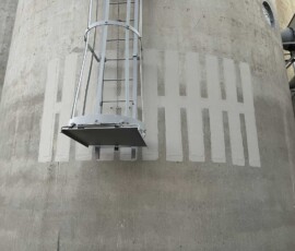 A ladder with a safety cage mounted on a large concrete industrial silo.