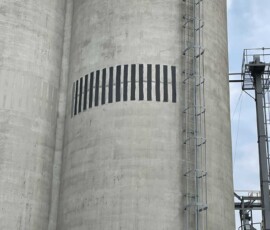 Large concrete grain silo with a vertical ladder and a series of dark horizontal vents.